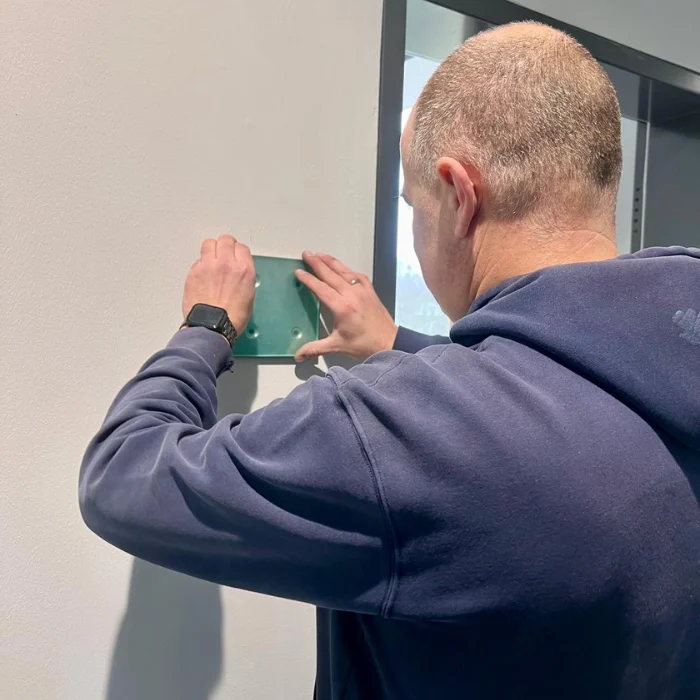 Handwerker bringt Türschild an, Detailaufnahme der Befestigung